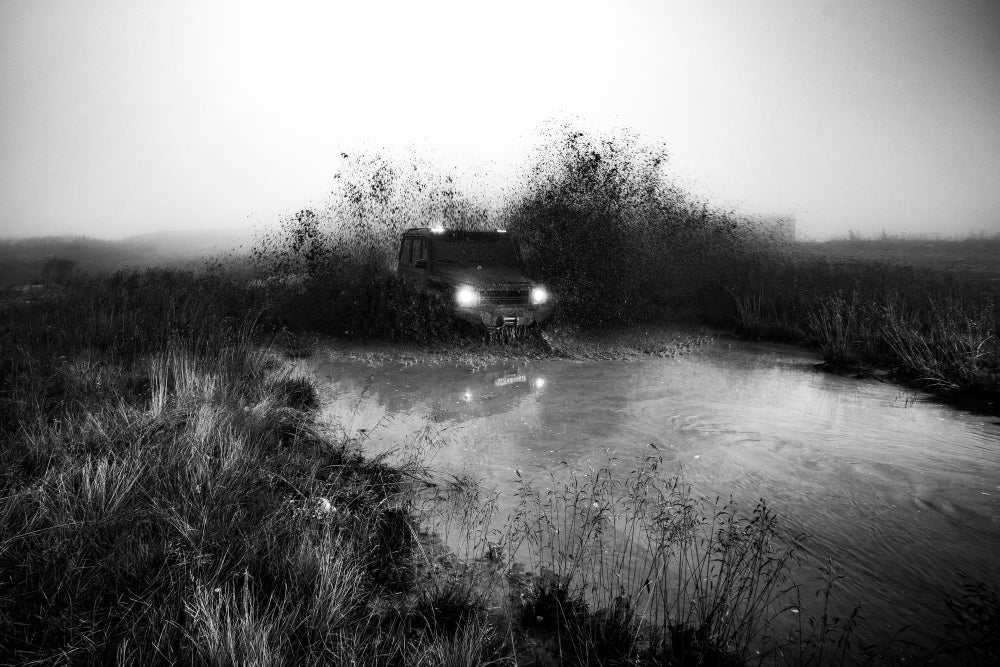 4x4 UTV driving aggressively through muddy terrain with splash in black and white