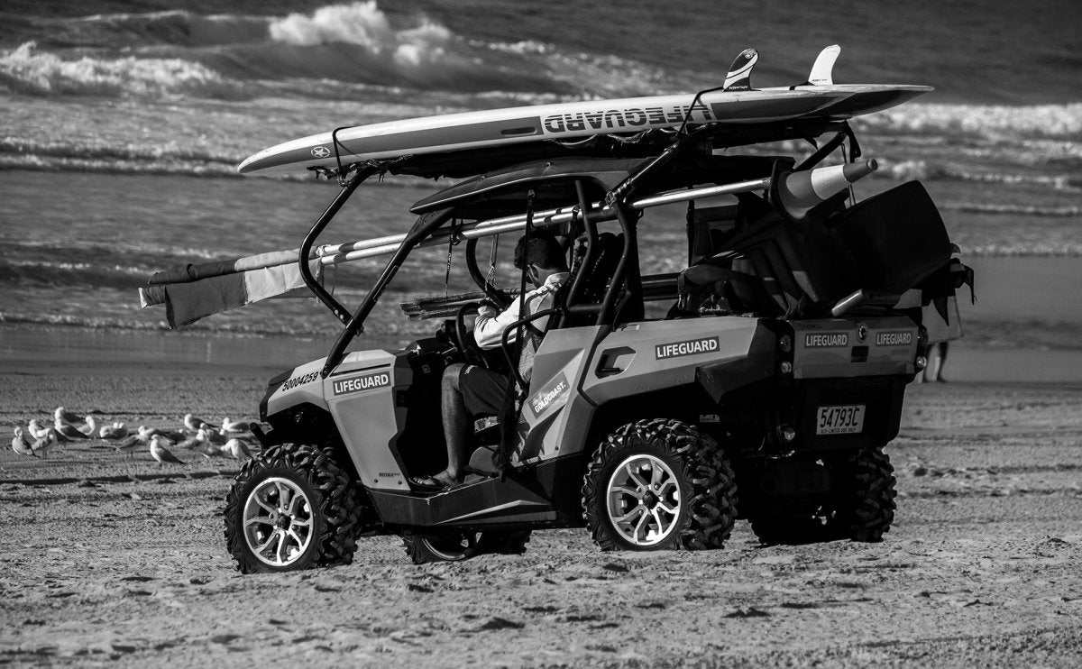UTV equipped with lifeguard gear and surfboards on sandy beach near ocean waves