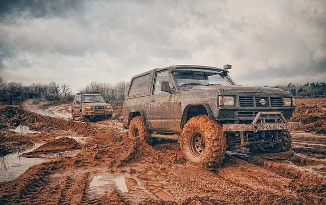 Two off-road vehicles driving through muddy terrain during an off-road race event