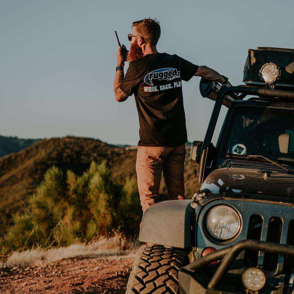 Man using GMRS off-road radio next to rugged vehicle in outdoor adventure setting