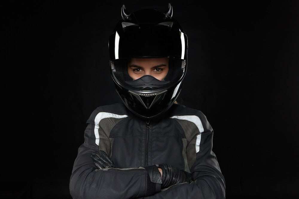 Woman wearing a properly fitted black motorcycle helmet and jacket with crossed arms against a black background