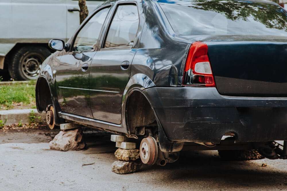 Car without wheels stolen and supported on rocks and blocks on street representing wheel theft risks and the need for wheel locks security.