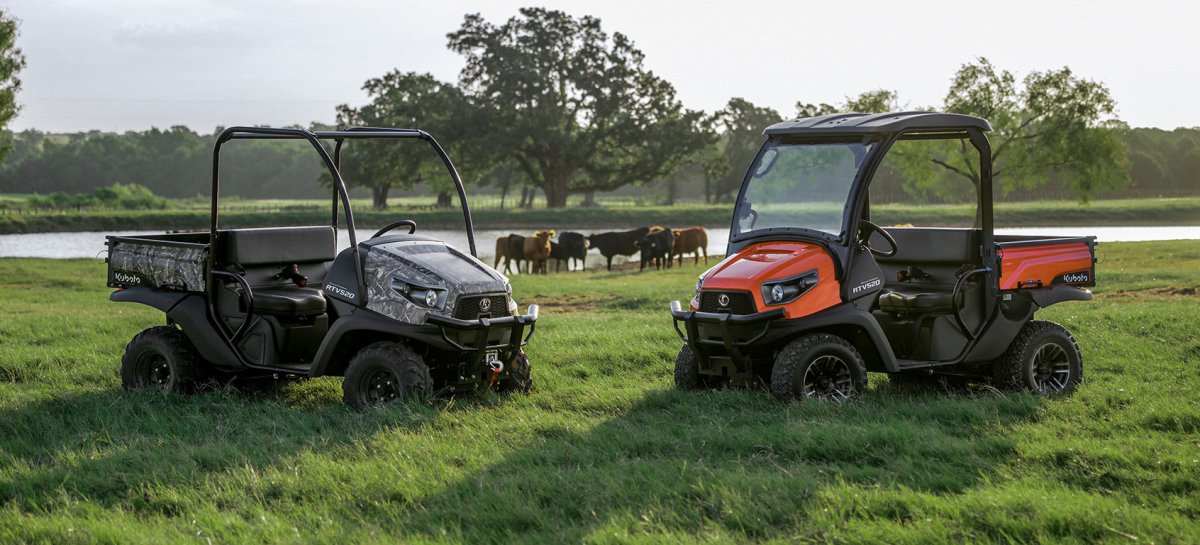 Two Kubota UTV utility vehicles parked on grassy farmland with cattle in background