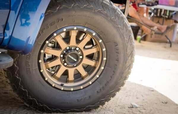 Bronze Raceline offroad wheel with beadlock design on rugged tire mounted on blue vehicle