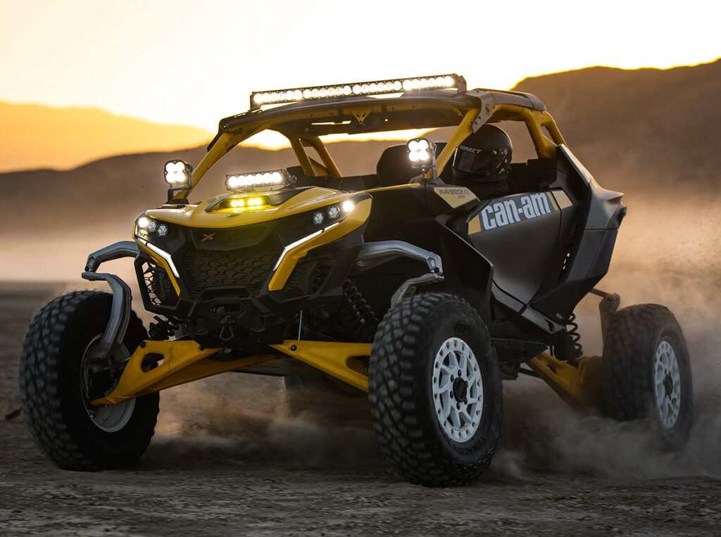 2024 Can-Am Maverick R yellow and black off-road side-by-side vehicle driving on dirt at sunset