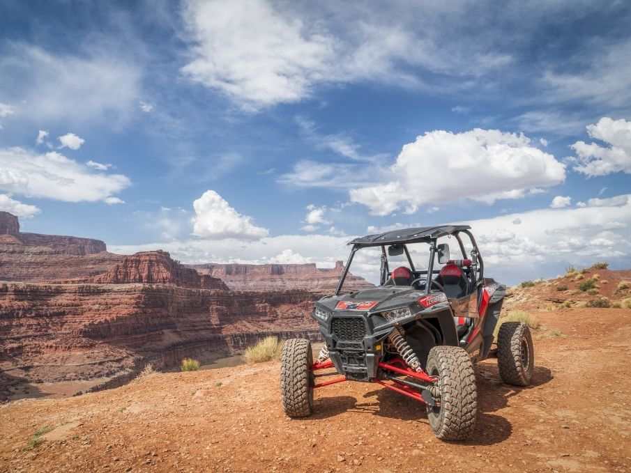 Polaris RZR XP 1000 UTV parked on rocky terrain with canyon background under blue sky