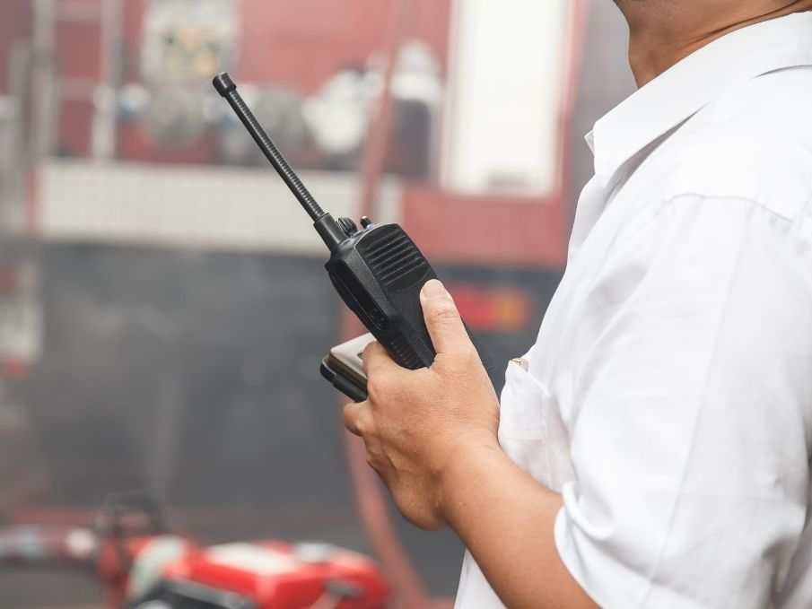 Person holding a black two-way radio with antenna outdoors