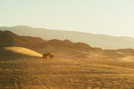 UTV riding fast across desert dunes with mountain background at sunrise