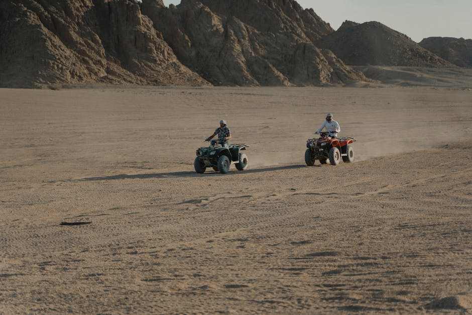 Two people riding side by side ATVs on a desert terrain near rocky mountains, illustrating off-road adventure with side by side parts.