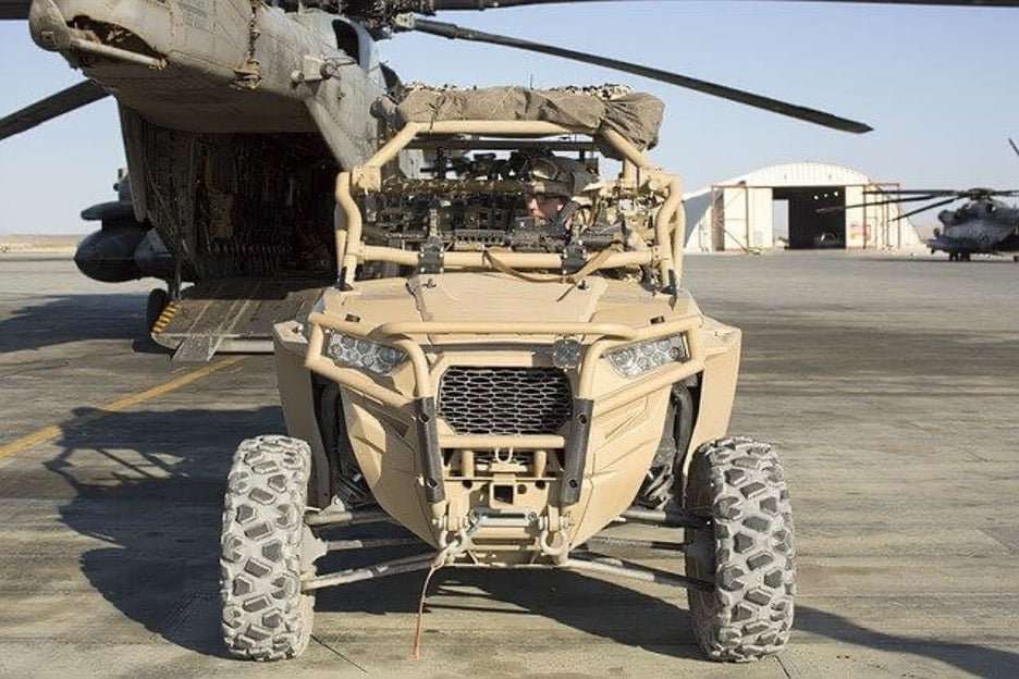 military UTV off-road vehicle parked with helicopters in the background