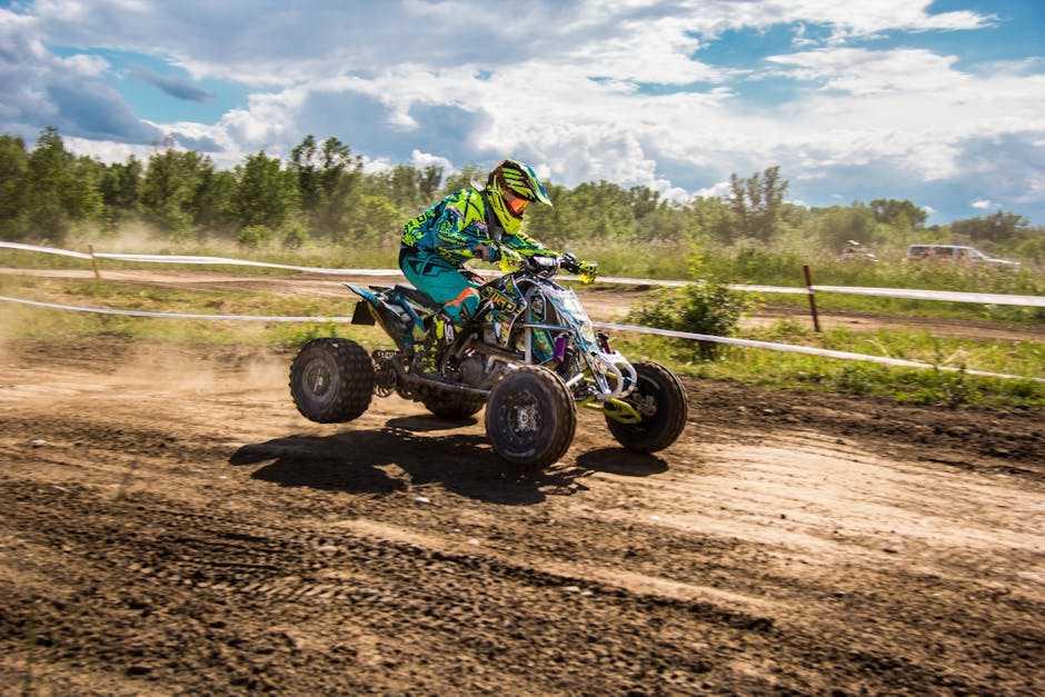 Rider on a Can-Am Maverick X3 all-terrain vehicle racing on a dirt track under a partly cloudy sky