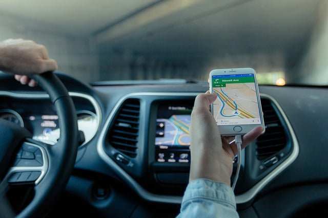 Person using smartphone with navigation app inside a vehicle dashboard showing map directions