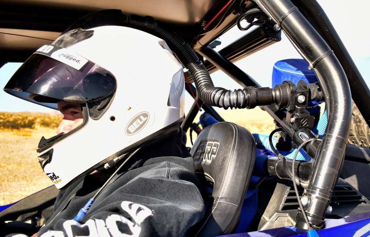 Off-road driver wearing a Bell racing helmet equipped with a fresh air helmet system connected to an air intake mounted on a roll cage in a UTV vehicle