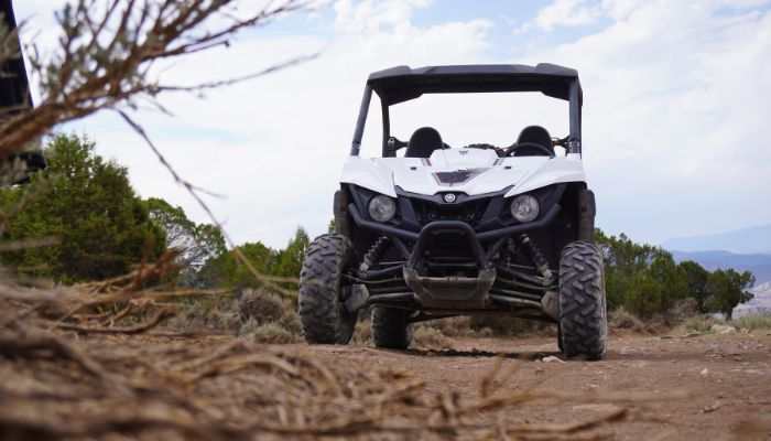 White CF Moto UTV off-road vehicle on rugged dirt trail with trees and cloudy sky background