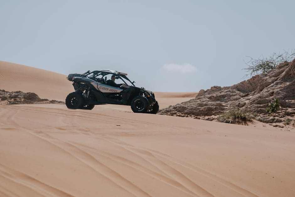 2024 Can-Am Commander off-road vehicle riding on sandy desert terrain near rocks and sparse vegetation