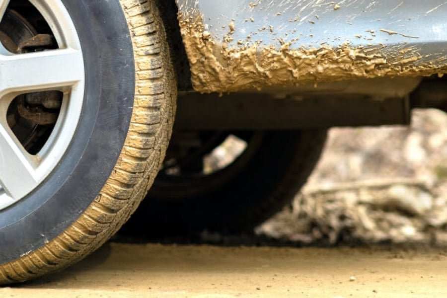 Close-up of UTV tire and wheel covered with yellow mud and dirt on muddy terrain