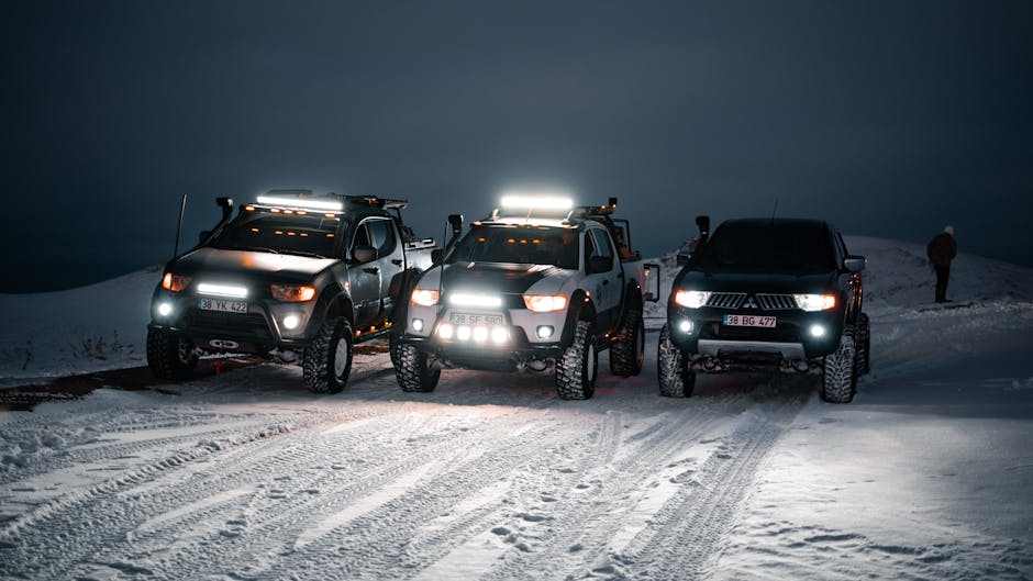 Three off-road vehicles equipped with bright UTV light bars driving on snowy terrain at night