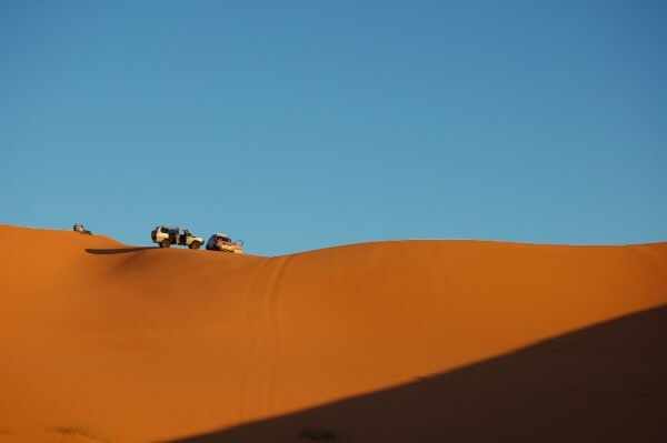 Off-road cars driving over large sand dunes under clear blue sky in desert environment