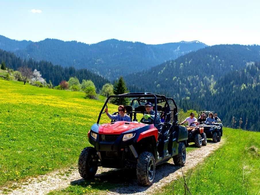 Group of people riding UTVs on a trail in a scenic mountainous area with green fields and clear blue sky, showcasing safety accessories for off-road vehicles