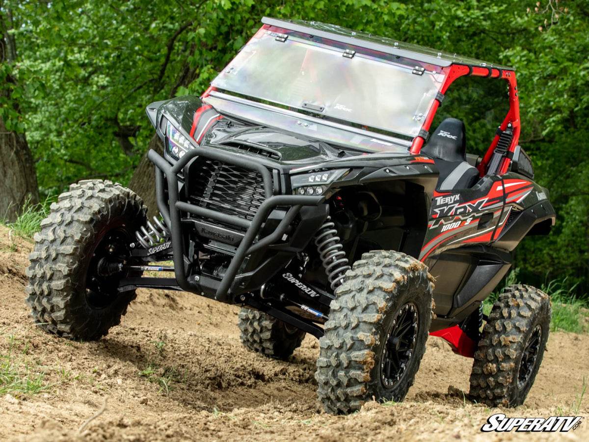 Red and black Kawasaki Teryx side-by-side all-terrain utility vehicle on muddy off-road trail with rugged tires and roll cage
